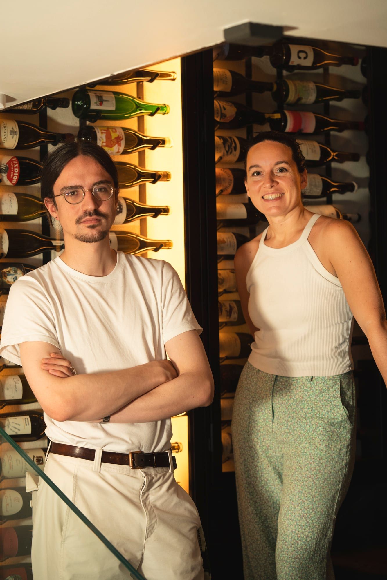 Julie and Côme in front of the wall of bottles